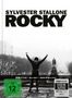 Text: "SYLVESTER STALLONE ROCKY", "FSK ab 12 freigegeben", "4K Ultra HD". Szene: Person hebt triumphierend die Arme auf einer Treppe., 1 Ultra HD Blu-ray und 2 Blu-ray Discs