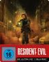 "Resident Evil" Text. FSK 16. Person mit Erste-Hilfe-Kasten rennt durch staubige Stadtstraße, Explosionen im Hintergrund.