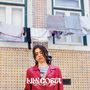LILY COSTA, Not Like You. Eine Person steht vor kachelverzierter Wand mit Wäscheleine. Sie trägt ein rotes Hemd., LP