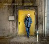 "MARKUS BECKER WINTER MOTION" steht über einem Mann vor einer gelben, abgenutzten Tür in einer alten Mauer.