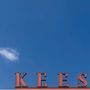 Der Text "KEES" in großen, roten Buchstaben vor einem klaren, blauen Himmel mit einer kleinen weißen Wolke.