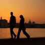 Zwei Personen gehen vor einem Sonnenuntergang, im Hintergrund eine Stadtsilhouette und ein Gewässer., LP