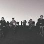 Eine Gruppe von Menschen fährt bei Dämmerung in einer Reihe auf Fahrrädern einen Hügel hinunter., LP