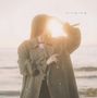 Der Text "singing" steht oben rechts. Eine Person in einem Mantel hält die Hand vor die Sonne an einem Strand., LP