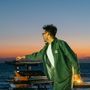 Ein Mann in grüner Jacke mit Herz-Logo steht an elektronischen Geräten vor einem Meer bei Sonnenuntergang., 2 LPs