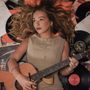 Eine Frau mit lockigem Haar liegt auf Schallplatten und hält eine Gitarre. Ein Notenblatt ist im Hintergrund sichtbar., CD