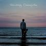 "Robin Katz Oceans for Eros" und "Orchestral Arrangements by Guy Barker". Ein Mann steht mit Gitarrenkoffer im Wasser bei Sonnenuntergang.