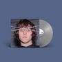 Eine graue Vinyl-Schallplatte und ihr Cover. Auf dem Cover ist das Gesicht einer Person mit überkreuzten silbernen Ketten., LP