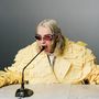 Kein sichtbarer Text. Person trägt gelbes Outfit aus Haftnotizen, spricht in ein Mikrofon, trägt rote Sonnenbrille., CD