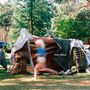 Text: "Hunt, Gather". Eine Kinderspielhütte aus Decken und Stöcken im Garten, ein Kind läuft daran vorbei., LP