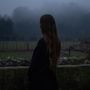 Lange Haare, dunkel gekleidet, steht eine Person vor einem nebligen Feld mit Bäumen im Hintergrund. Stimmung ruhig und düster., LP
