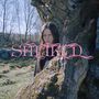 Text: "SMEKKIÐ" in pinker Schrift. Eine Person steht hinter einem Baum in einer Waldlandschaft., LP