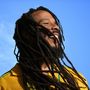 Ich kann den Text nicht erkennen. Ein Mann lächelt vor einem klaren blauen Himmel, trägt Dreadlocks und ein gelbes Hemd., CD