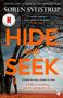 „HIDE AND SEEK“ steht in großen Buchstaben zentral. Ein Kind lehnt an einem Baum. Alles in Blau- und Rottönen., Buch
