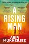 "A Rising Man" von Abir Mukherjee. Silhouette eines Mannes in Kolonialuniform vor einem gelb-orangefarbenen Hintergrund., Buch