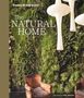 Text: "HANS BLOMQUIST", "The NATURAL HOME", "photography by DEBI TRELOAR". Szene: Grünes Pflanzenwand, brauner Sessel, weiße Lampen., Buch