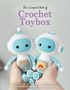 "The Compact Book of Crochet Toybox. Everything you need to start creating today." Zwei gehäkelte Roboter in Händen gehalten., Buch
