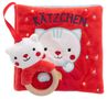 Text: "KÄTZCHEN". Rotes Kinderbuch mit Katzengesicht und Plüschanhänger in Kätzchenform, Holzring darunter., Buch