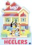 "Bluey" und "Zuhause bei den Heelers" in großer Schrift. Eine fröhliche Hunde-Familie steht vor einem bunten Haus., Buch