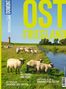 Texte: "OSTFRIESLAND", "AKTIV MIT PADDEL UND PEDAL", "WATTWANDERN ZWISCHEN ZWEI WELTEN", "KNISTERNDE KLUNTJE URGEMÜTLICHE TEETIED". 

Eine grüne Wiese mit Schafen, einem Wassergraben und einem Leuchtturm im Hintergrund., Buch