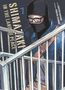 Texte „SHIMAZAKI IN THE LAND OF PEACE“, „Story Gouten Hamada“, „Zeichnungen Takeshi Seshimo“. Person mit Maske und Brille., Buch