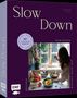"Slow Down" - Ein Buch über Soulfood-Rezepte; eine Frau kocht in einer gemütlichen Küche mit frischem Obst und Blumen., Buch