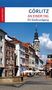 Titel: "Görlitz an einem Tag – Ein Stadtrundgang". Eine belebte Straße in Görlitz, rechts ein Uhrturm, links ein Brunnen., Buch
