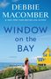 Titel: "Debbie Macomber: Window on the Bay". Frau in Hut neben Rad, blickt aufs Meer. Gelbes Haus, blauer Himmel., Buch