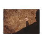 Keine Texte sichtbar. Ein Mann steht vor einer felsigen Wand, trägt Sonnenbrille und hat die Arme verschränkt.