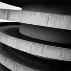 Keine Texte vorhanden. Eine spiralförmige Parkhausrampe mit Betonwänden in Schwarz-Weiß.