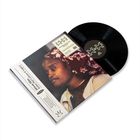 Eine Person mit einem roten Kopftuch mit weißem Blumenmuster und einer hellen Jacke, betrachtet von der Seite.