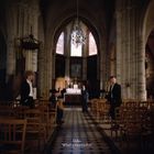 Text: "Hallan What’s a Heaven For?" Menschen in einer Kirche, sitzend oder stehend, mit hohen Decken und bunten Fenstern.