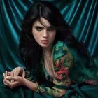 Es gibt keinen Text im Bild. Eine Frau mit langen dunklen Haaren posiert vor einem türkisfarbenen Stoffhintergrund.