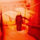 Unleserlich, verschwommenes Logo über einem orange-roten Hintergrund mit unscharfer Gestalt auf einer Treppe.