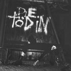 "Die Todin" steht in weißer Graffiti-Schrift auf Holz. Darunter sitzt eine Person auf einer Bank, nachdenklich und ruhig.