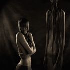 Zwei Personen mit langen Haaren verdecken das Gesicht, eine sitzt, die andere steht. Dunkle, stimmungsvolle Beleuchtung.