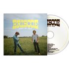 "BRISCOE - HEAT OF JULY" steht in großen gelben und schwarzen Buchstaben. Zwei Männer stehen auf einer Wiese.