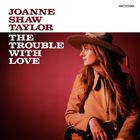 JOANNE SHAW TAYLOR, THE TROUBLE WITH LOVE. Eine Frau mit Hut und Gitarre, schaut nach rechts, vor rotem Hintergrund.