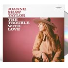 "JOANNE SHAW TAYLOR" und "THE TROUBLE WITH LOVE". Eine Frau mit Hut hält eine Gitarre und blickt nach rechts.