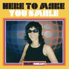 „HERE TO MAKE YOU SMILE“ steht oben. Unten „CHLOÉ CAILLET“. Eine Frau mit Sonnenbrille lächelt vor buntem Hintergrund.