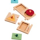 Text „montessori“. Vier Holzpuzzle-Elemente mit bunten Formen: ein roter Kreis, ein gelbes Dreieck und quadratische Einsätze.