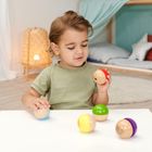 Ein Kind spielt an einem Tisch mit bunten Holzhalbkugeln, im Hintergrund ein Bett und eine Lampe.