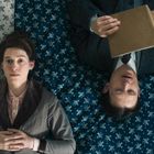 Zwei Personen liegen auf einem geblümten Bett. Eine Frau schaut zur Decke, ein Mann liest ein Buch.