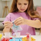 Ein Mädchen in einem rosa T-Shirt hält eine Packung auf der "Jelly Play" steht. Vor ihr sind bunte Spielzeuge.