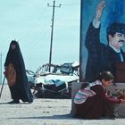 Eine Frau kniet vor einem Wandgemälde eines salutierenden Mannes neben einem Straßenschild auf einer ländlichen Straße.