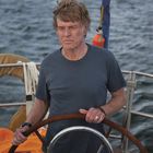 Ein älterer Mann steuert ein Boot auf offenem Wasser, sein Gesicht ist konzentriert.