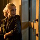 Eine Frau lehnt nachdenklich gegen eine Tür und blickt zur Seite. Sie ist in warmes Licht getaucht.