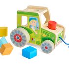 Text "HABA" auf einem grünen Holzauto mit bunten Formen: gelber Zylinder, blaues Dreieck, oranger Würfel, blauer Würfel.