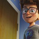 Ein fröhlicher Junge mit großer Brille steht in einem Raum. Er trägt ein Shirt mit "RC" Logo. Regal voller Bücher.