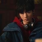 Ein junger Mensch in rotem Hoodie und blauer Jacke trägt Kopfhörer um den Hals. Der Blick ist ernst, im Hintergrund ist ein Bücherregal.